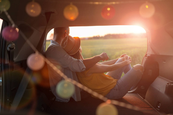 A fiatal pár ül a saját autó törzs, és nézze a naplementét - Fotó, kép