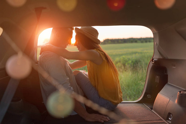 Young couple sitting in their car trunk and watching the sunset - Fotografie, Obrázek