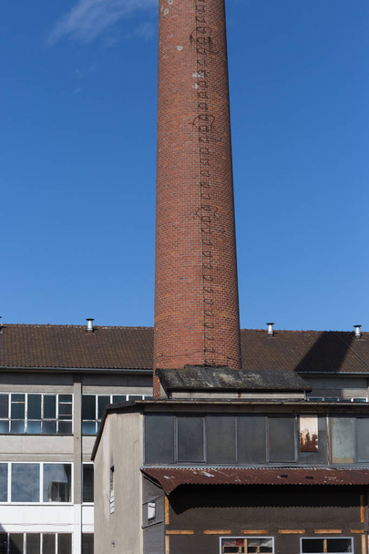in una giornata molto soleggiata a giugno nel sud della Germania si vede l'architettura più antica di una zona industriale in disuso con camino e finestre e facciate schiantate che necessitano di ristrutturazione
 - Foto, immagini