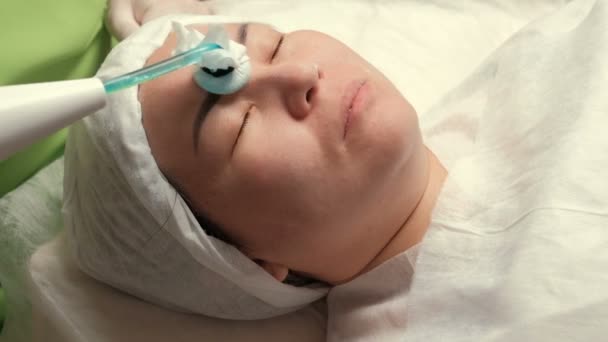 Darsonvalization. Közelkép az arc, a fizioterápiás arcfiatalító eljárást egy ázsiai nő. Kozmetikus eszközzel a pulzáló váltakozó áram a magas frekvenciájú. Aktiválás a vérkeringést, a szövetek nutritio javítása - Felvétel, videó