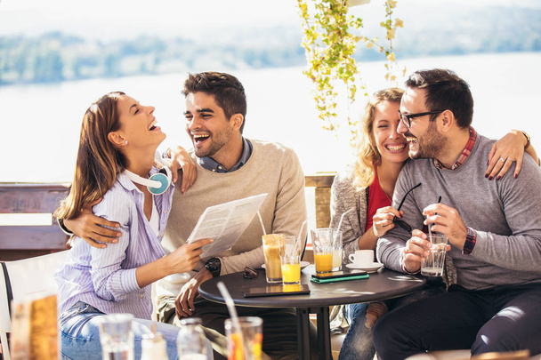 Группа из четырех друзей веселятся за чашечкой кофе вместе. Две женщины и двое мужчин в кафе смеются и наслаждаются своим временем - Фото, изображение