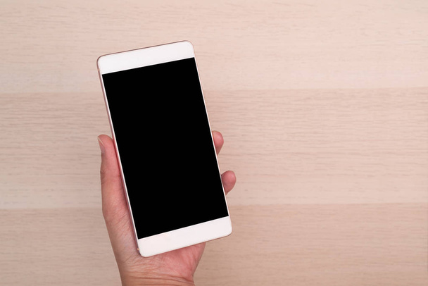 hand holding smartphone with blank screen isolated on wooden background - 写真・画像