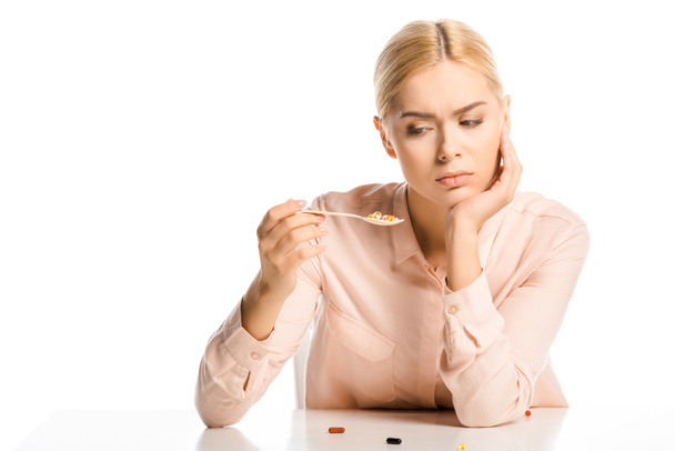 müde attraktive Frau sieht Pillen auf Löffel isoliert auf weiß - Foto, Bild