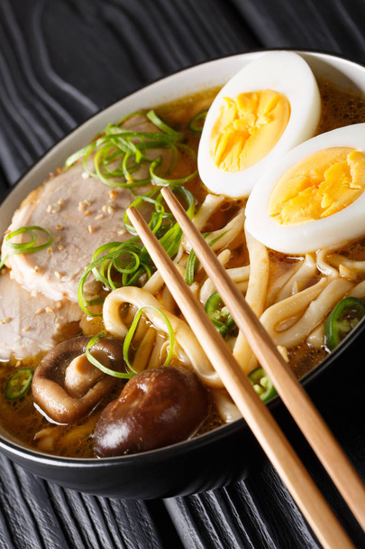 Pyszne udon japoński zupa z wieprzowiny, jaj, chabru i cebuli zbliżenie w misce na stole. Vertica - Zdjęcie, obraz