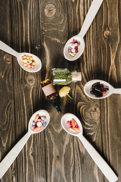 top view of spoons with pills and glass bottles with alternative medicines on wooden tabletop - Photo, Image