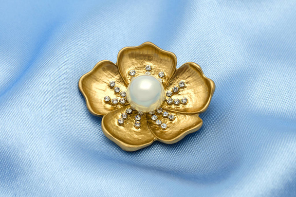 Χρυσή καρφίτσα λουλούδι με ένα μαργαριτάρι και πολύτιμοι λίθοι που απομονώνονται σε μετάξι - Φωτογραφία, εικόνα