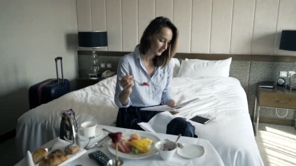 Young pretty businesswoman reading magazine and eating breakfast in hotel - Footage, Video
