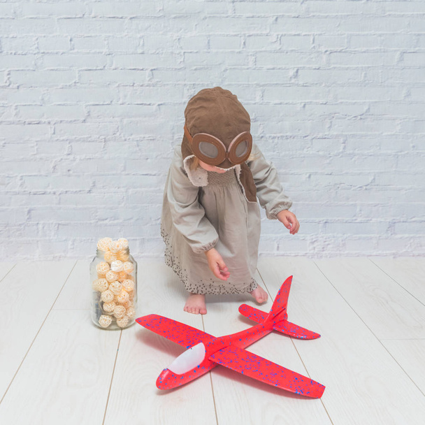 a girl, child in the helmet of the pilot with the aircraft and lights in the glass in front of a white brick wall - Fotoğraf, Görsel