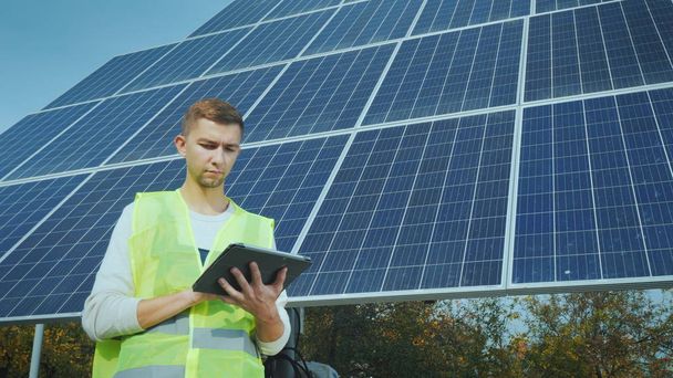 Un jeune ingénieur en vêtements de travail travaille avec une tablette près d'un grand panneau solaire
 - Photo, image