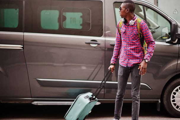 African american man in checkered shirt, sunglasses and earphones with suitcase and backpack. Black man traveler against van car. - Fotoğraf, Görsel