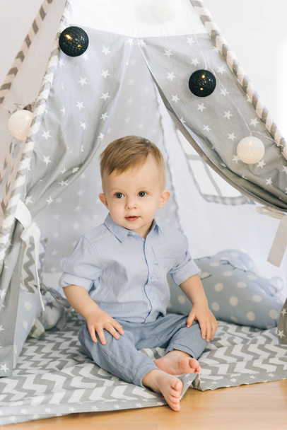 Cute one year old baby playing in a tent, wigwam. Shadow depth of field, natural light. The interior of the children's room is grey, blue and white - Valokuva, kuva