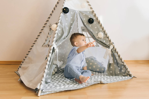 Cute one year old baby playing in a tent, wigwam. Shadow depth of field, natural light. The interior of the children's room is grey, blue and white - Photo, Image