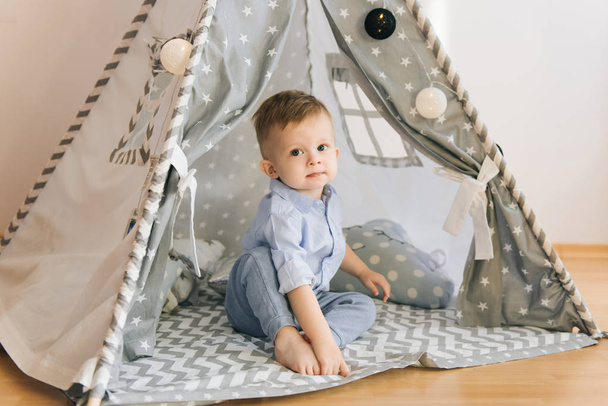 Cute one year old baby playing in a tent, wigwam. Shadow depth of field, natural light. The interior of the children's room is grey, blue and white - Fotoğraf, Görsel