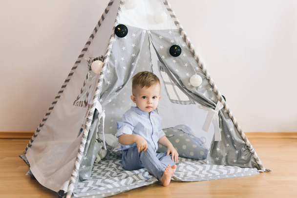 Cute one year old baby playing in a tent, wigwam. Shadow depth of field, natural light. The interior of the children's room is grey, blue and white - Foto, immagini