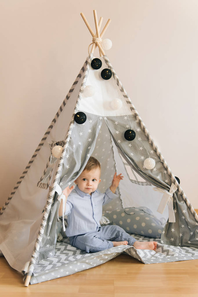 Cute one year old baby playing in a tent, wigwam. Shadow depth of field, natural light. The interior of the children's room is grey, blue and white - Fotó, kép