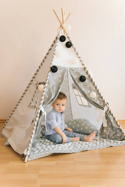 Cute one year old baby playing in a tent, wigwam. Shadow depth of field, natural light. The interior of the children's room is grey, blue and white - Fotó, kép