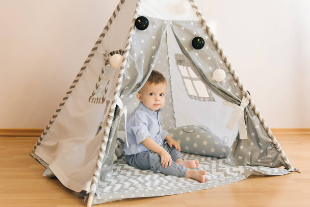 Cute one year old baby playing in a tent, wigwam. Shadow depth of field, natural light. The interior of the children's room is grey, blue and white - Foto, immagini