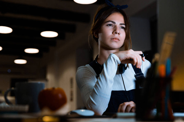 Εικόνα του συμπυκνωμένου νεαρή γυναίκα κάθεται σχεδιαστής στο γραφείο που εργάζεται με το tablet και τον υπολογιστή το βράδυ. - Φωτογραφία, εικόνα
