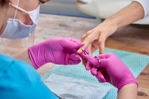 Selective focus of skilled manicurist cutting cuticle with scissors to woman. - Foto, Bild
