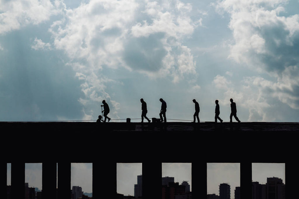 Silhouettes of workers making roof repairs on a cloudy day - Foto, Bild
