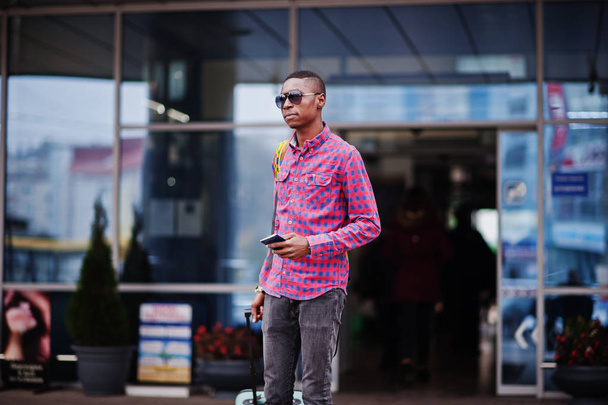 African american man in checkered shirt, with suitcase and backpack. Black man traveler against bus station. - Fotó, kép