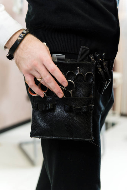 Closeup view of the work belt and tools worn by a hairdresser in the hair salon. A hairdresser's hand choosing from a variety of professional cutting instrument - 写真・画像
