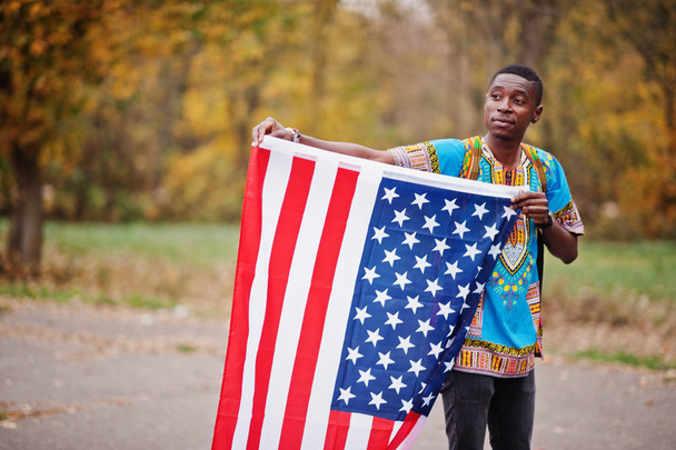 African man in africa traditional shirt on autumn park with USA flag.  - Foto, imagen