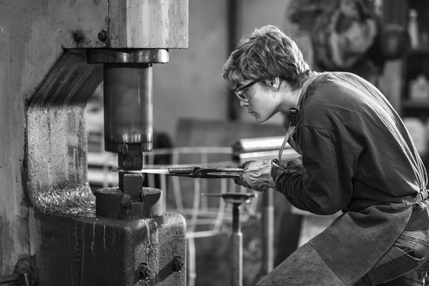 Fémet gazdaságban a penész fogóval szakember előrehajolva koncentrációja nézni a munkáját a műhelyben dolgozó fiatal blaksmith - Fotó, kép