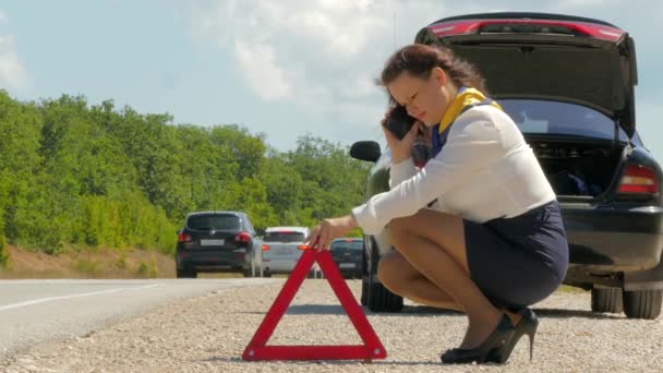 Mujer sentada junto a un coche roto y hablando por teléfono móvil
 - Metraje, vídeo
