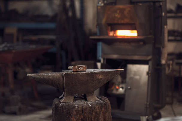 Σφύρα στο ένα αμόνι μπροστά από ένα κόκκινο καυτός burning φούρνων σε ένα εργαστήριο μεταλλουργίας ή σιδεράς - Φωτογραφία, εικόνα