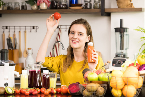 Υγιή, νεαρή γυναίκα σε μια κουζίνα με φρούτα και λαχανικά και χυμό - Φωτογραφία, εικόνα