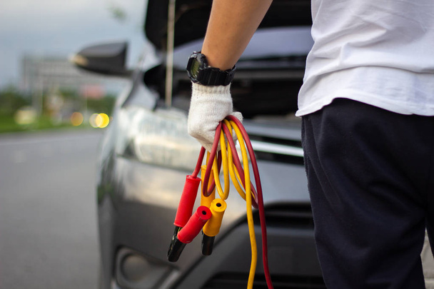 Car mechanic man holding battery jumper cables to charge a dead battery - Foto, afbeelding