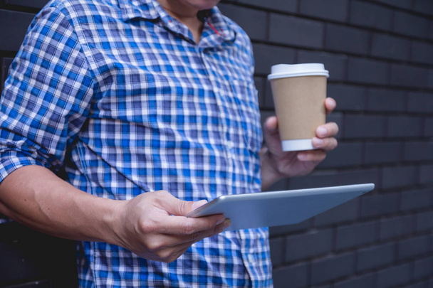 Young man using tablet computer holding coffee cup on street wall with copy space - Fotoğraf, Görsel