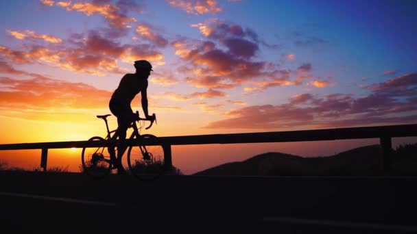 Sziluettjét a kerékpáros a naplementét a hegyek között - Felvétel, videó