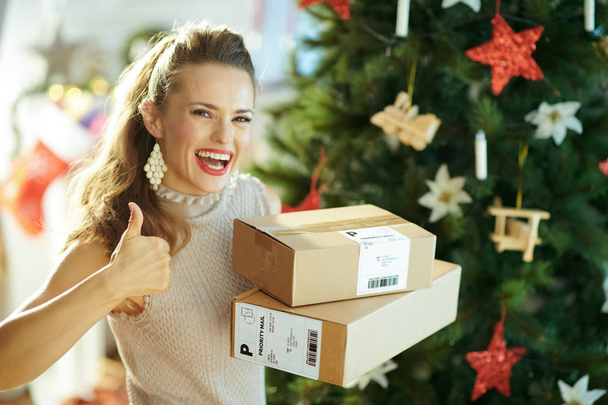 happy stylish woman with parcels showing thumbs up near Christmas tree - Zdjęcie, obraz