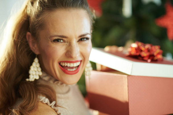 Portrait of happy modern housewife near Christmas tree opening Christmas present box - Foto, immagini