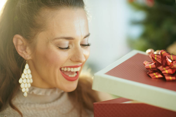 happy young woman near Christmas tree looking inside Christmas present box - Foto, afbeelding