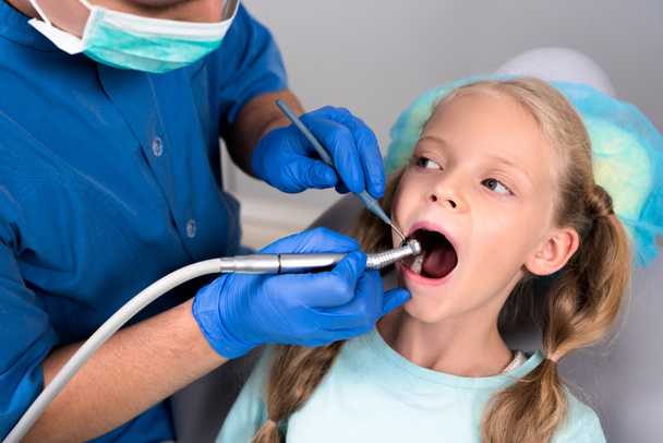 dentista con pieza de mano dental trabajando con dientes de niño pequeño
 - Foto, Imagen
