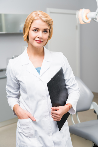 beautiful young dentist with clipboard standing in office - Fotoğraf, Görsel