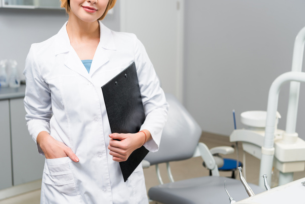 cropped shot of young dentist with clipboard standing in office - Фото, изображение