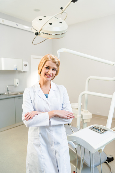 beautiful young dentist with crossed arms looking at camera in office - Foto, Imagem