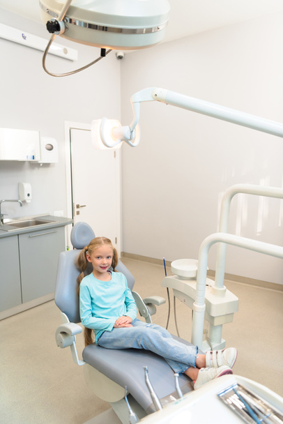 высокий угол обзора очаровательного маленького ребенка, сидящего в стоматологическом кресле в кабинете стоматолога
 - Фото, изображение