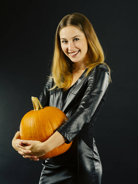 Photo of a young sexy woman holding a pumpkin over dark background for Halloween. - Fotografie, Obrázek