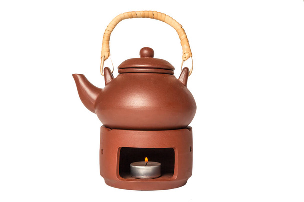 Una tetera de arcilla marrón con un mango de madera se encuentra en un soporte con una vela de calefacción. Concepto de ceremonia del té oriental
 - Foto, imagen