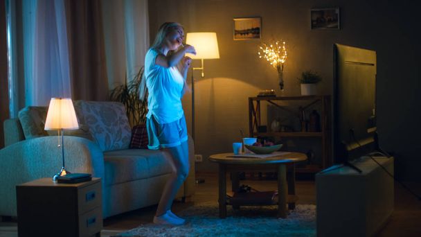 In the Evening Beautiful Woman Happily Dances in Her Living Room while Watching TV, Also She Holds Smartphone. - Φωτογραφία, εικόνα