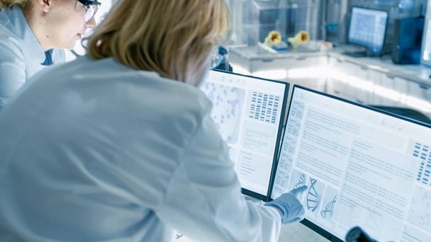 Senior Female Scientist Discusses Scientific Data with Her Laboratory Assistant. They're looking at Two Displays in a Modern Laboratory. - Foto, afbeelding