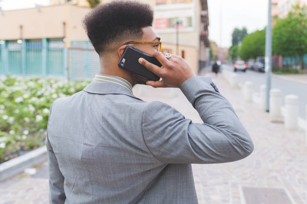 Genç siyahi iş adamı dışarıda akıllı telefonlardan konuşuyor. Konuşma, cevap verme, iş görüşmesi konsepti. - Fotoğraf, Görsel