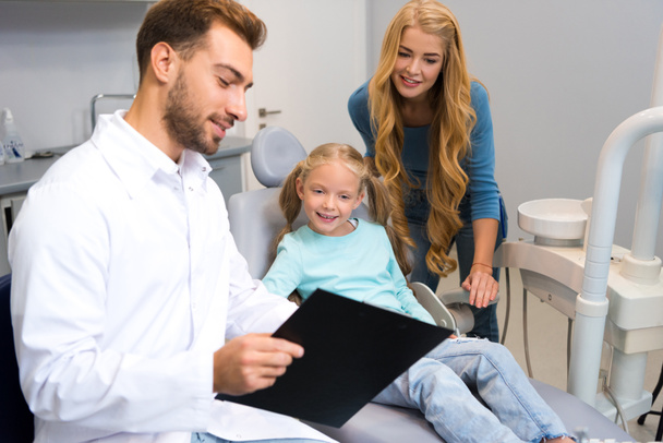 dentist showing clipboard to mother and little daughter - Valokuva, kuva