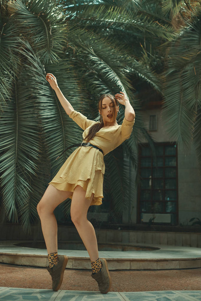 An active young hip hop dancer dancing on tropical plants background, big palm leaves outdoors. Jungle outfit. Movement is life. - Photo, image
