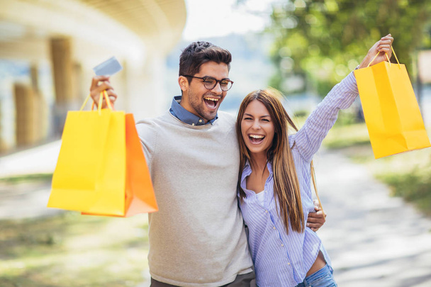 Porträt eines glücklichen Paares mit Einkaufstüten nach einem Einkauf in der Stadt, lächelnd und mit Kreditkarte - Foto, Bild